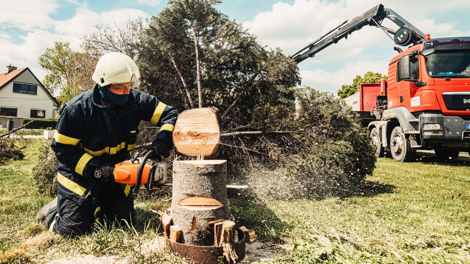 Firefighter using chainsaw to cut tree trunk with red truck in background