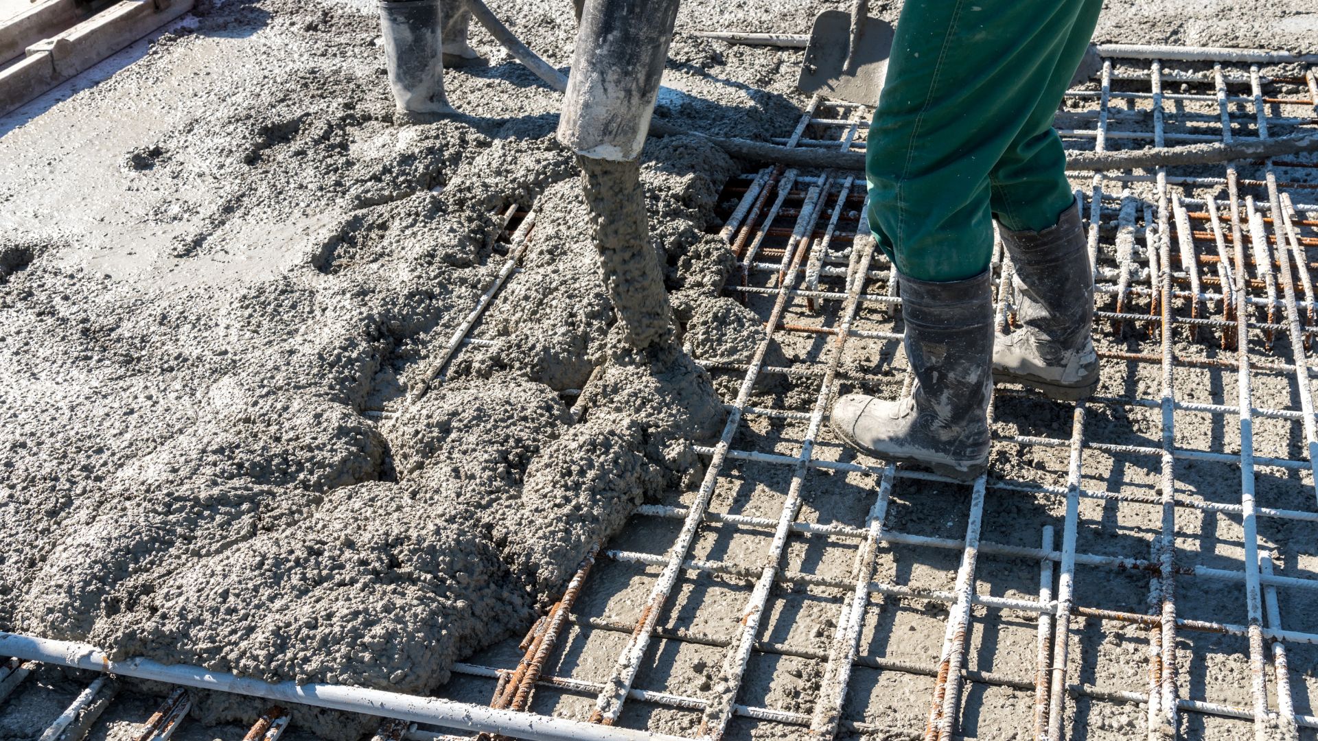 Construction worker pouring concrete over steel rebar foundation grid