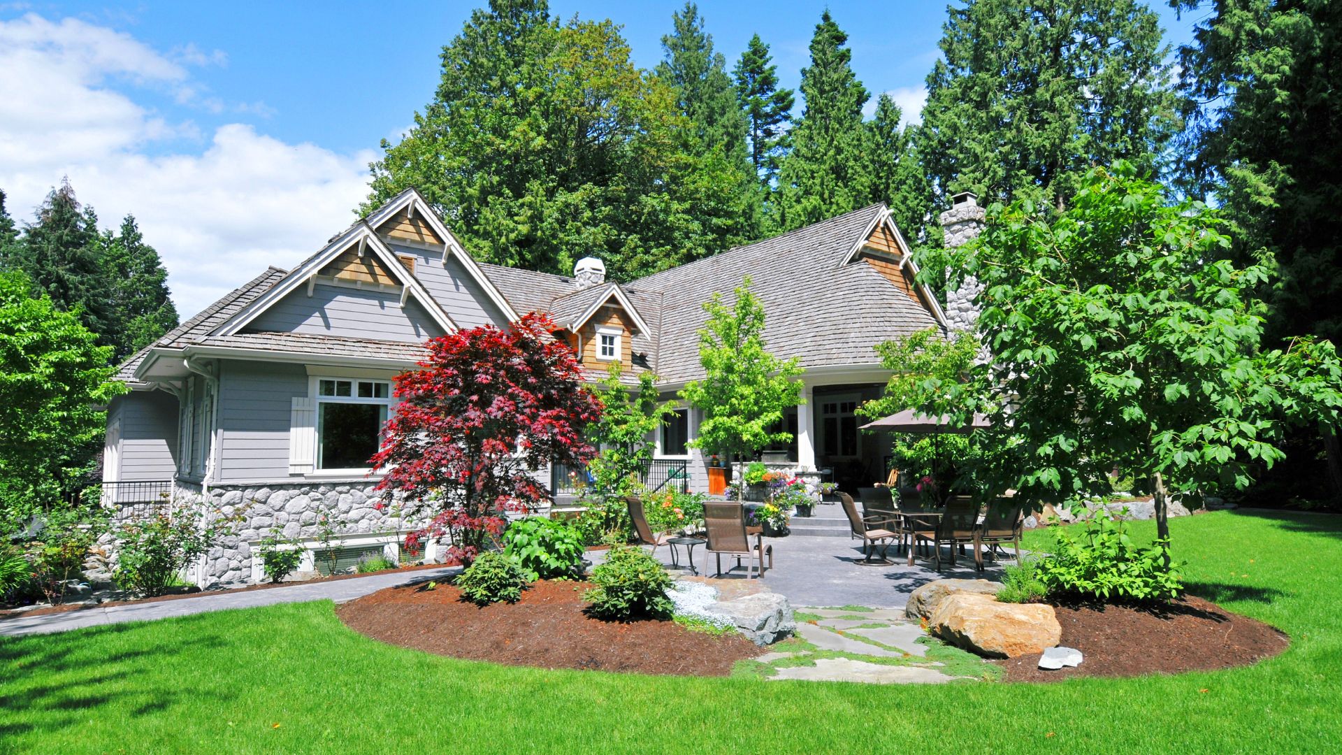 Spacious stone and wood house with manicured lawn and red flowering tree