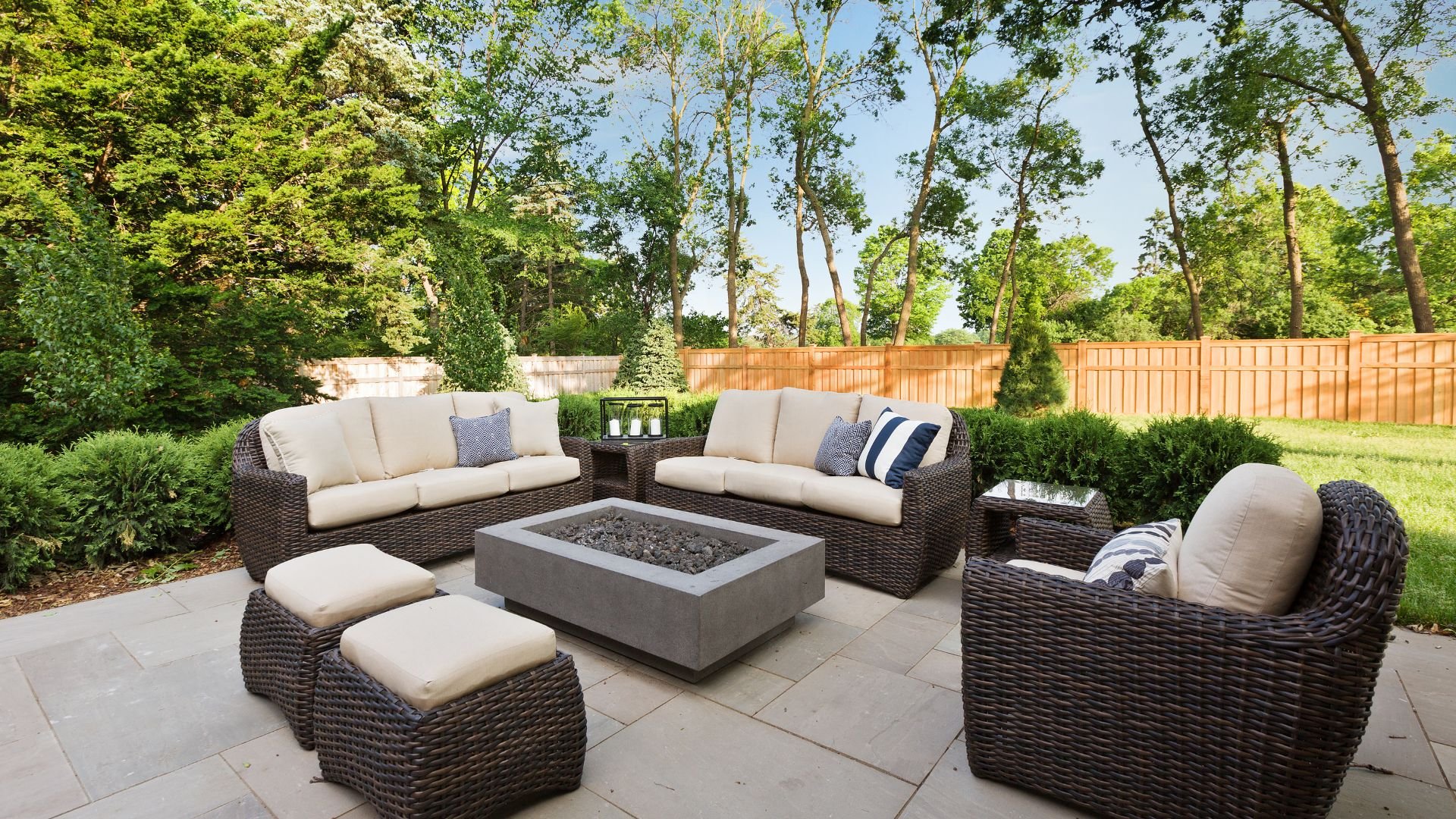 Outdoor patio with wicker furniture, fire pit, and lush green backyard